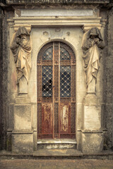 Fototapeta premium Weathered Mausoleum Entrance with Mourning Statues and Ornate Door