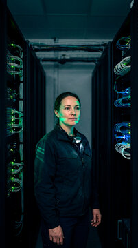 Confident female engineer standing among glowing server racks in modern data center