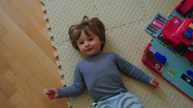 Toddler lying beside toy vehicles on play mat at home, childhood leisure moment highlighting imagination, independent play, learning and development
