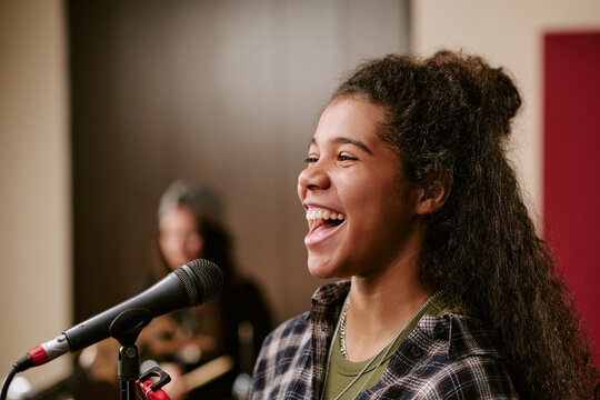 Close up of biracial teenage girl singing into microphone during band rehearsal, performing live music concept. Ideal for youth music education, talent promotion, entertainment marketing
