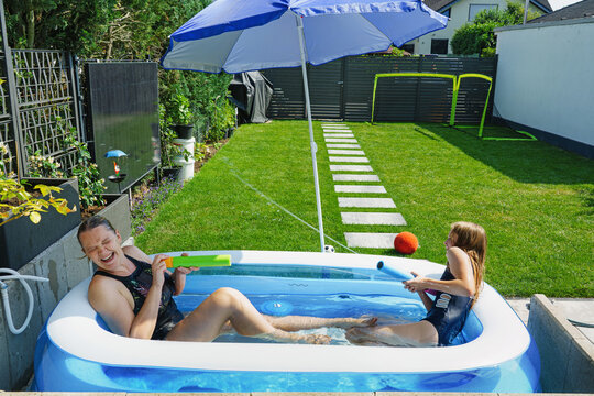 Escaping the heat and cooling off at home &ndash; a happy family splashing each other in a small garden pool.