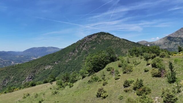 Montagne verdi e pendii erbosi che si estendono verso montagne boscose sotto un cielo limpido. Un paesaggio naturale ampio e luminoso che unisce profondit&agrave;, tranquillit&agrave; e variet&agrave; vegetativa