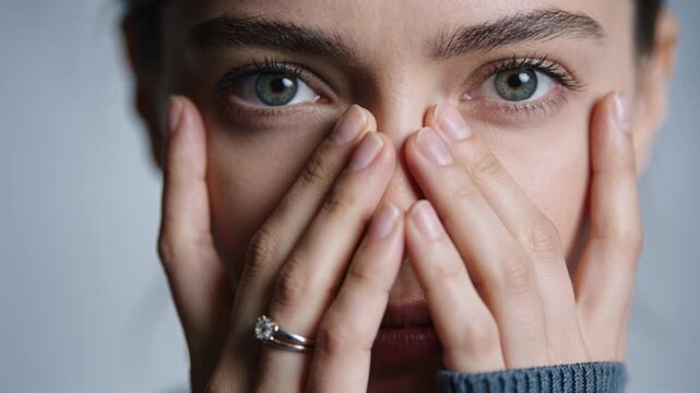 Holding woman covering face with hands in gray sleeve, fingers sliding, eyes staring, diamond ring