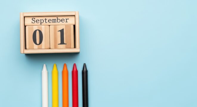 September 1st wooden calendar blocks and colorful crayons on a light blue background