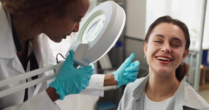 Dermatologist examines patient skin under magnifier. Bright lamp highlights careful examination in clinic with cosmetology care and healthcare consultation. Theme shows trust and professionalism.