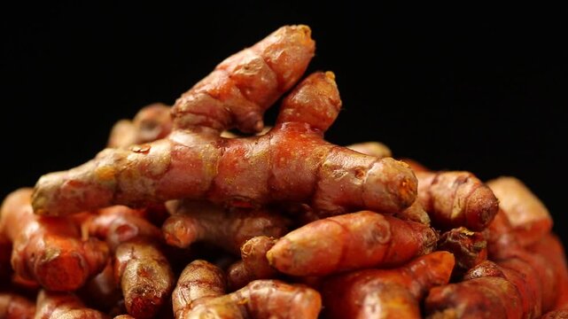 Pile of fresh raw yellow turmeric roots slowly rotating on black background, traditional Thai herb.