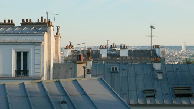 A slow camera tilt up showcasing the classic gray zinc rooftops, clay chimneys, and television antennas of historic Parisian apartments.