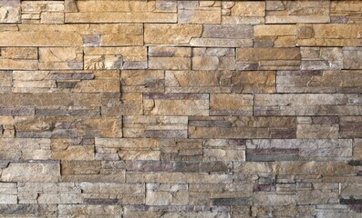 Naklejka premium Wall made of reconstructed strips stone with warm tones ranging from beige to ochre, all the way to gray and reddish shades. Rustic coating for outdoor or indoor. Background and texture. Full frame.