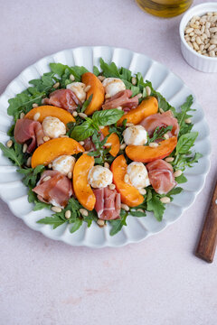 Fresh salad made with arugula, fresh peaches, prosciutto, mini mozzarella cheese, arugula, and toasted pine nuts, drizzled with balsamic glaze. Healthy dining and Mediterranean cuisine concepts.