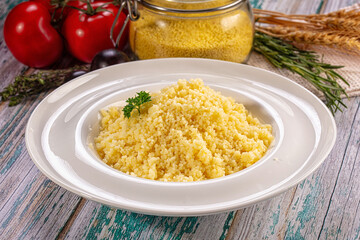 Obraz premium Cooked couscous on white plate with fresh tomatoes and herbs on rustic wooden table