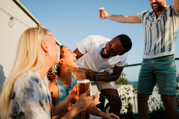 Diverse friends laughing and enjoying a rooftop party with beer