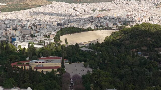 High angle establishing shot of Panathenaic Stadium and Zappeion Hall surrounded by urban sprawl in Athens, Greece showing Ardittos Hill and sprawling cityscape