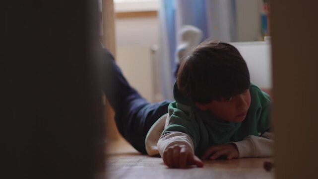Young boy lying on bedroom floor at home looking bored and disengaged, highlighting childhood downtime, quiet moments, contemplation and everyday family life
