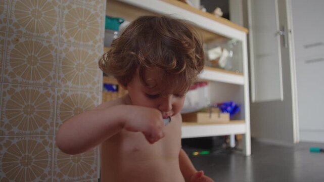 Toddler eating independently from bowl while sitting on kitchen floor at home, highlighting self feeding skills, childhood development