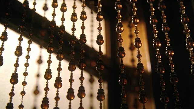 Swaying bead curtain shifting from small sway in front of glazed panel, catching warm backlight