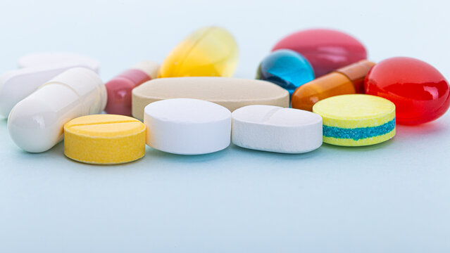 Assorted tablets, capsules, and softgels arranged on a light blue background. Healthcare and pharmaceutical concept for medication and wellness.
