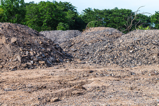 Gravel piles at an outdoor construction site with trees in the background. Industrial material concept for building, road work, infrastructure, and land development.