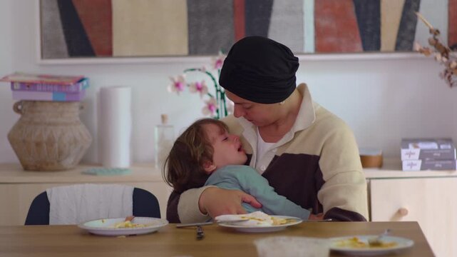 Mother comforting crying toddler at dining table in family home during cancer recovery, highlighting maternal care, emotional support, attachment, resilience and family connection