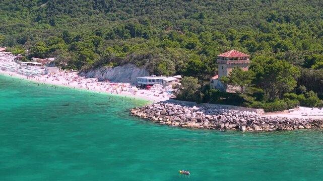 Portonovo Marche Italy 4k drone 70mm sea view of Torre Clementina watchtower. Authentic hidden gem of white beach resort under green Monte Conero hills tropical turquoise water b-roll