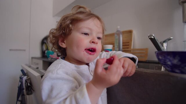 Toddler enjoying fresh berries during snack time in family kitchen, highlighting healthy nutrition, childhood development, independence and everyday domestic life
