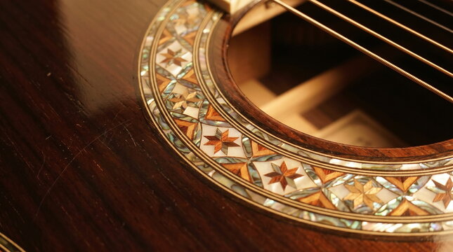 Macro close-up of an acoustic guitar soundhole featuring an ornate geometric rosette inlay crafted from wood and shimmering abalone shell