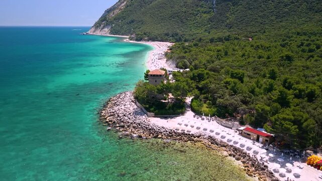 Portonovo Marche Italy 4k drone of Torre Clementina watchtower. Aerial flyover through pine trees from beach to beach toward historic Santa Maria church coast. best beaches hidden gems