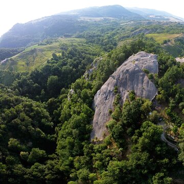 An aerial view showcases the imposing Sasso di Sant'Andrea, a prominent sandstone geological feature surrounded by dense forest. Zocca, Modena, Emilia-Romagna, Italy