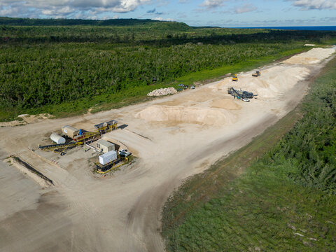 Aerial view of the restoration of North Field Base showing industrial equipment, large sand piles, and dirt roads in Northern Tinian, Tinian, Northern Mariana Islands.
