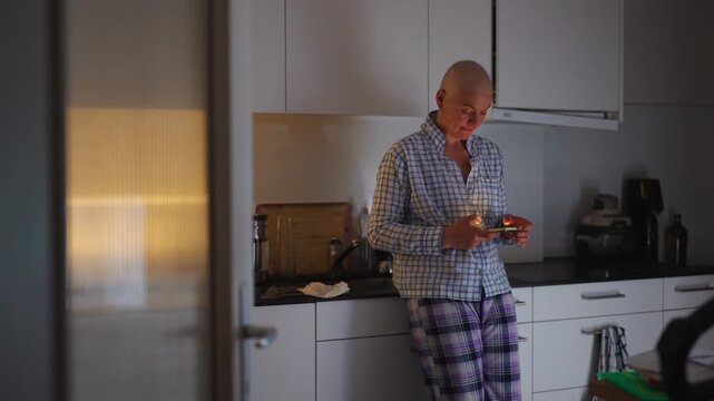 Female cancer patient using smartphone in kitchen at home during recovery journey, highlighting communication, independence, resilience, connection and everyday life