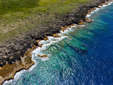 Aerial view of Chigit Beach with rugged volcanic rock formations, turquoise coastal waters, and lush green vegetation in Northern Tinian, Tinian, Northern Mariana Islands.
