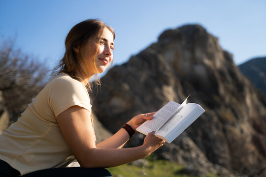 Young woman enjoying a book while sitting in a mountain landscape. Relaxation, learning and peaceful moments in nature.