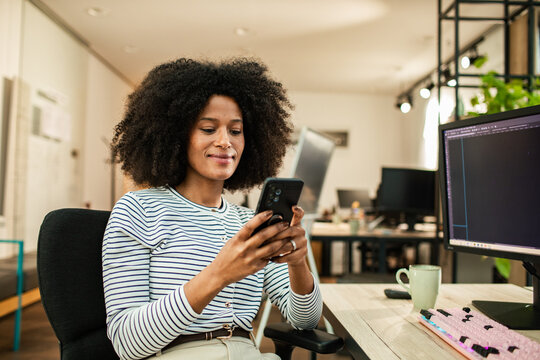 Smiling professional woman using smartphone at desk in modern office