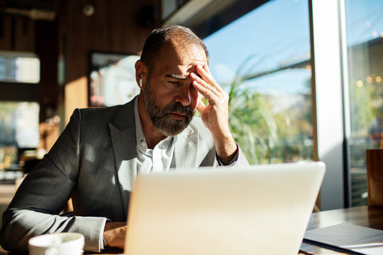 Mature businessman stressed at laptop in cafe