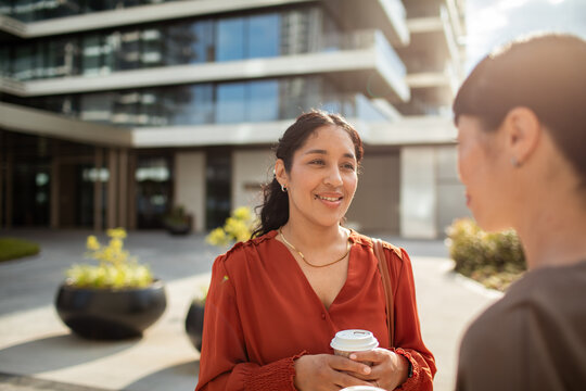 Two coworkers chatting with coffee outside modern office building