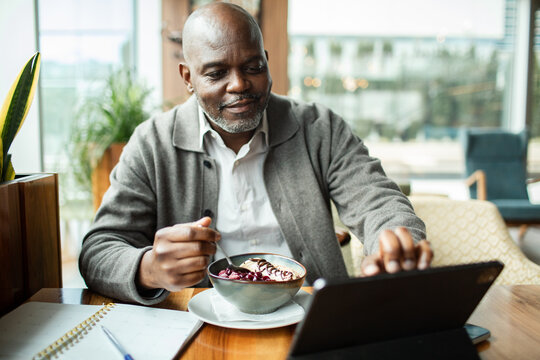 Mature man eating breakfast bowl and using tablet at cafe