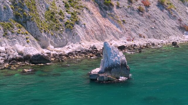 Portonovo Marche Italy 4k drone 70mm orbit flight of Vela sail rock 360 view. Aerial parallax curve over cliff revealing canoe and distant wild beach under vertical white rocks coast b-roll