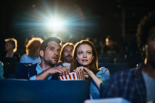 Couple watching a movie and sharing popcorn in a movie theater