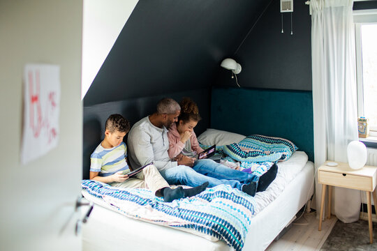 Father and children using tablets in bedroom