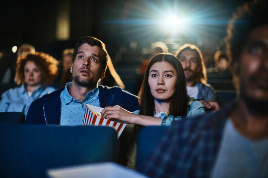 Young couple watching suspenseful movie in cinema