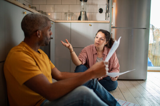 Concerned couple discussing household bills on kitchen floor