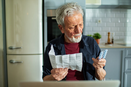 Senior man reading medication instructions at home kitchen