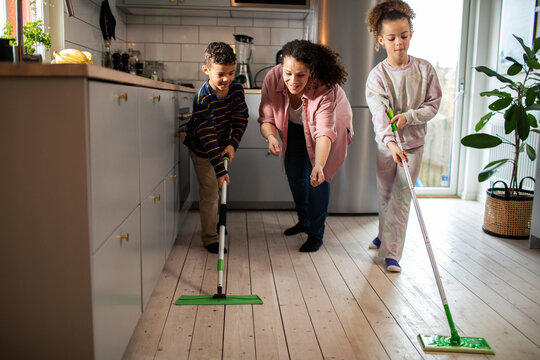 Mother helping children mop kitchen floor at home