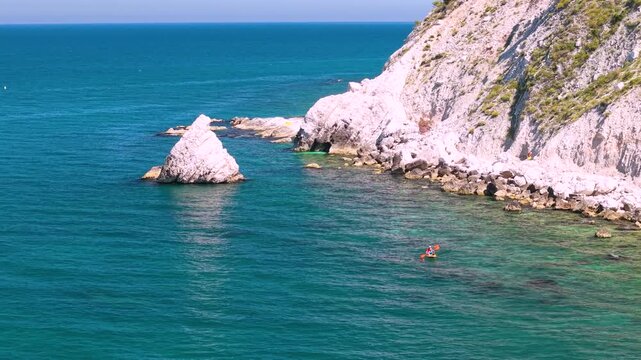 Portonovo Marche Italy 4k drone 70mm close up of Vela sail rock. Flight toward sailboat with canoe in tropical turquoise sea water near Monte Conero coast summer travel b-roll