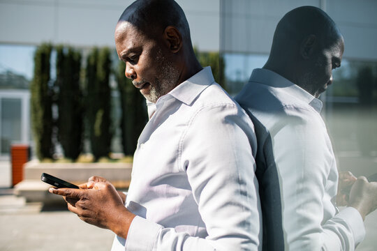 Mature man using smartphone by glass wall outdoors