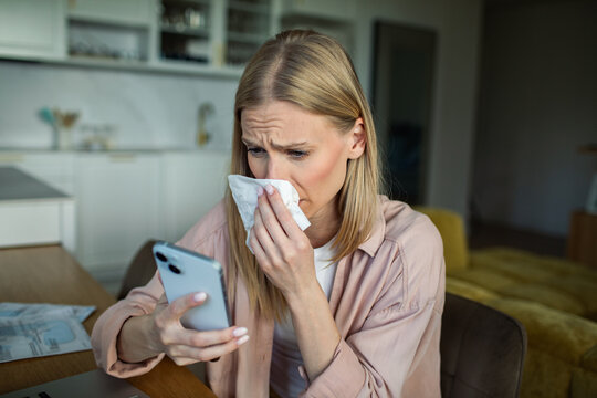 Sick woman with tissue checking smartphone at home
