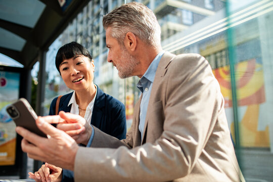 Business colleagues discussing smartphone at city bus stop