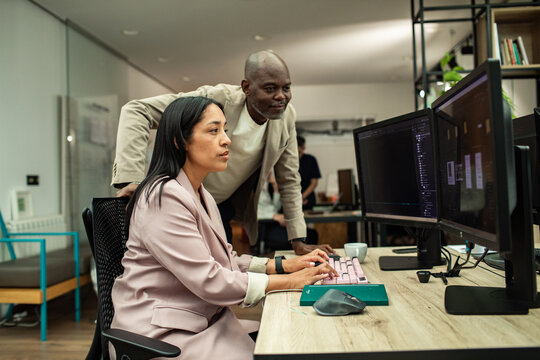 Coworkers collaborating at dual monitors in modern office