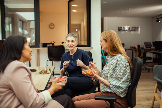 Coworkers eating lunch and chatting in modern office