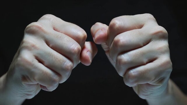 Clenching adult fists at start, making small shifts on black backdrop, showing knuckles for study