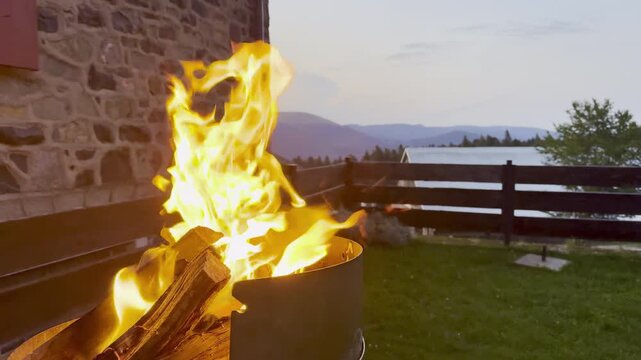 Crackling campfire burning in a metal fire pit at dusk by a stone